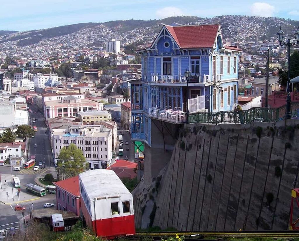 Imagen destacada de Valparaíso, una casa azul y un funicular en primer plano, con la ciudad de Valparaíso al fondo, revelando su belleza única y su energía creativa.